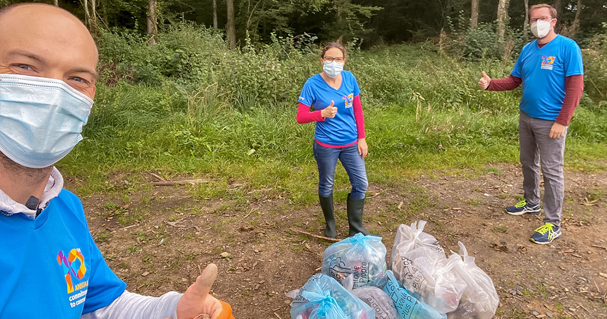 2 men and a woman wearing face masks and blue Commitment to Community shirts, volunteering to clean up trash.