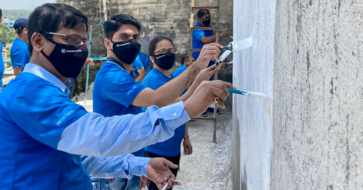 People wearing face masks painting outside of building, wearing blue Commitment to Community shirts.